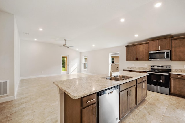 kitchen with light stone counters, stainless steel appliances, ceiling fan, sink, and a center island with sink