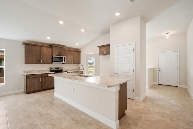 kitchen with appliances with stainless steel finishes, vaulted ceiling, a kitchen island with sink, sink, and light tile patterned floors