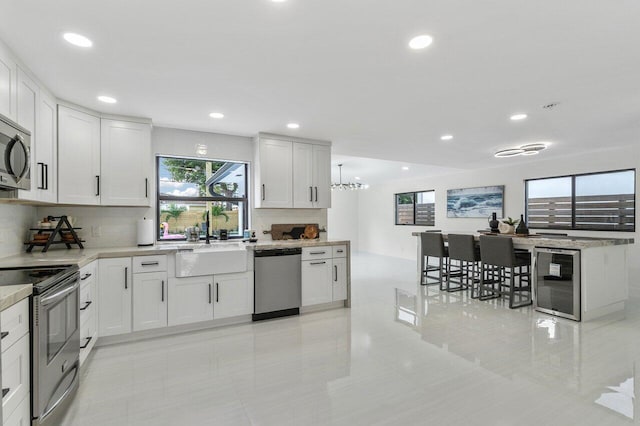 kitchen featuring appliances with stainless steel finishes, tasteful backsplash, beverage cooler, light tile patterned floors, and white cabinetry