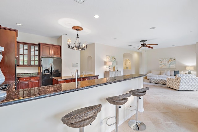 kitchen featuring dark stone counters, ceiling fan with notable chandelier, decorative light fixtures, and stainless steel refrigerator with ice dispenser