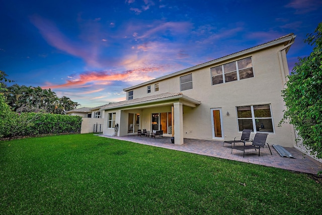 back house at dusk featuring a patio area and a yard