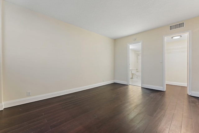 unfurnished bedroom featuring connected bathroom, dark wood-type flooring, a textured ceiling, a walk in closet, and a closet