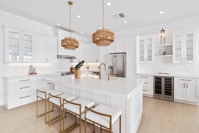 kitchen with high end refrigerator, ornamental molding, beverage cooler, a center island with sink, and white cabinets