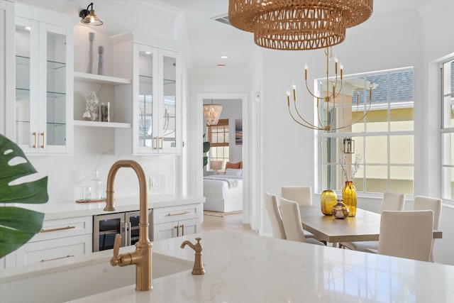 kitchen with light stone counters, white cabinets, ornamental molding, and an inviting chandelier