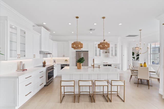 kitchen with a breakfast bar, appliances with stainless steel finishes, a center island with sink, and decorative light fixtures