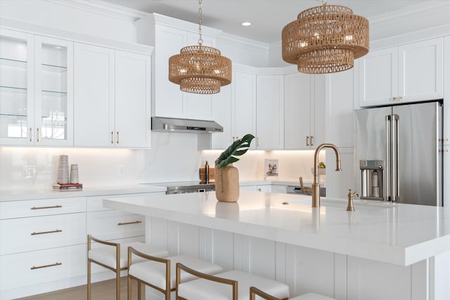 kitchen with high end refrigerator, white cabinetry, a kitchen island with sink, and range hood