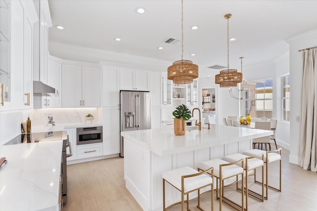 kitchen with high end fridge, pendant lighting, a kitchen bar, a center island with sink, and white cabinets