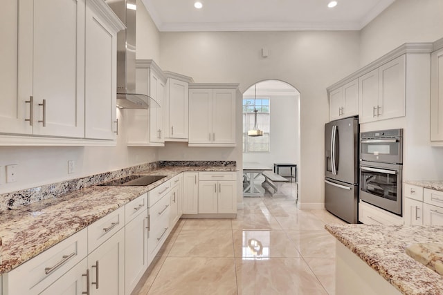 kitchen with arched walkways, stainless steel appliances, light stone countertops, wall chimney exhaust hood, and crown molding