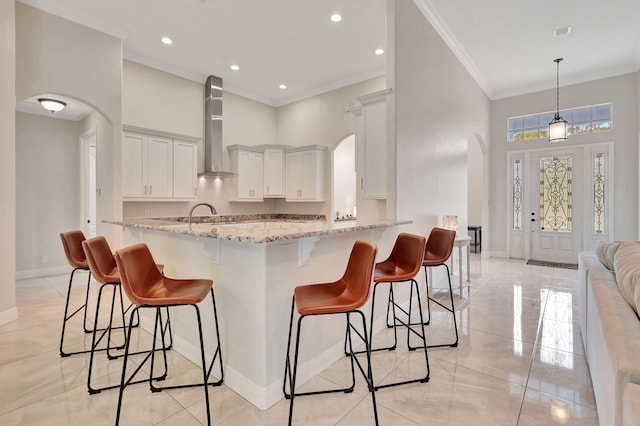 kitchen featuring wall chimney exhaust hood, light stone counters, and kitchen peninsula