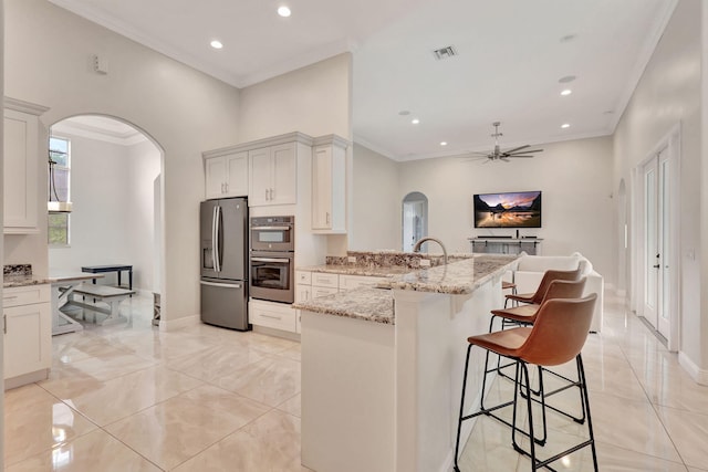 kitchen with arched walkways, stainless steel appliances, a peninsula, visible vents, and a kitchen breakfast bar