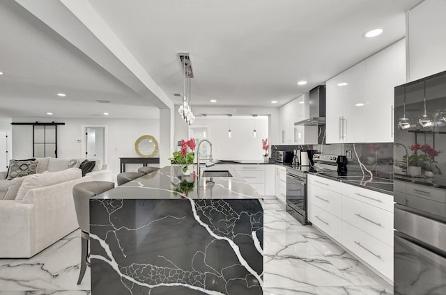 kitchen featuring stainless steel range with electric stovetop, wall chimney exhaust hood, a barn door, white cabinetry, and hanging light fixtures