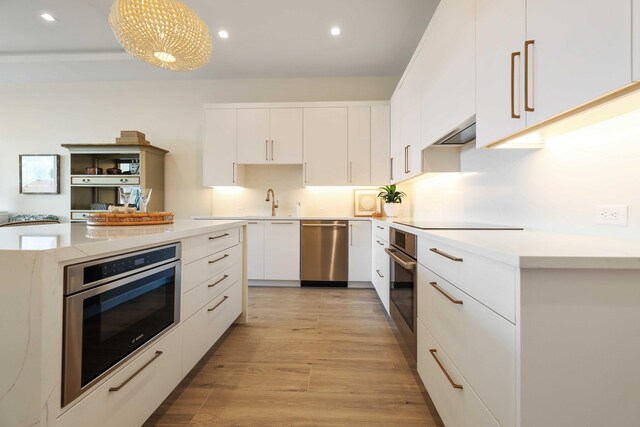 kitchen featuring ventilation hood, stainless steel appliances, white cabinets, a kitchen island, and light hardwood / wood-style flooring