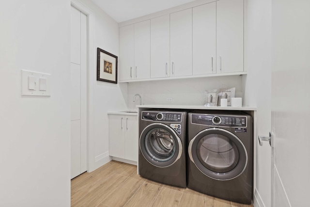 laundry room with sink, washing machine and dryer, light wood-type flooring, and cabinets