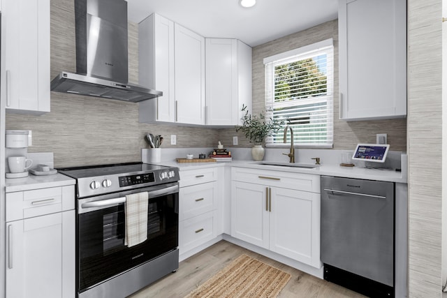 kitchen with appliances with stainless steel finishes, wall chimney exhaust hood, sink, light hardwood / wood-style flooring, and white cabinets