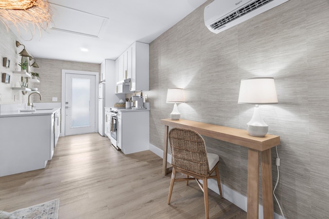 kitchen featuring light wood-type flooring, white appliances, a wall unit AC, sink, and white cabinetry