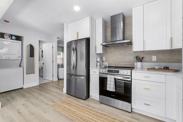 kitchen featuring white cabinets, stacked washer / dryer, wall chimney range hood, and stainless steel appliances