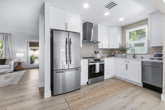 kitchen featuring sink, wall chimney exhaust hood, appliances with stainless steel finishes, white cabinets, and light wood-type flooring