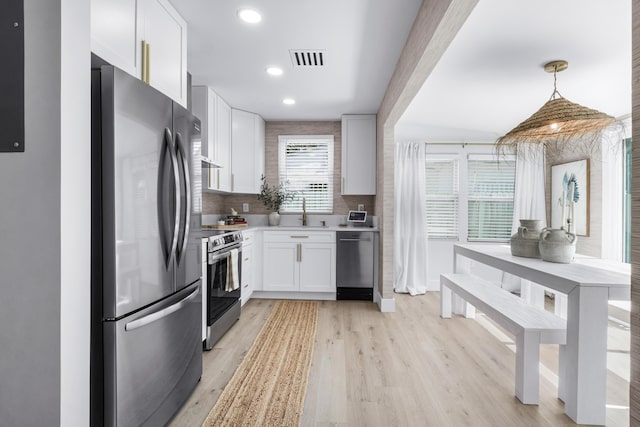 kitchen featuring light hardwood / wood-style flooring, decorative light fixtures, decorative backsplash, white cabinets, and appliances with stainless steel finishes