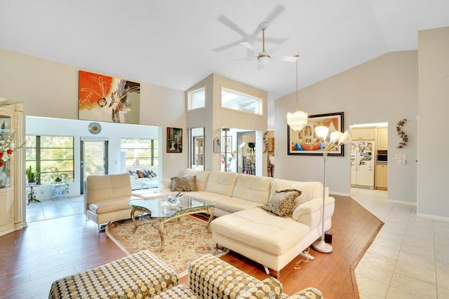 living room featuring high vaulted ceiling, light wood-style flooring, baseboards, and ceiling fan with notable chandelier