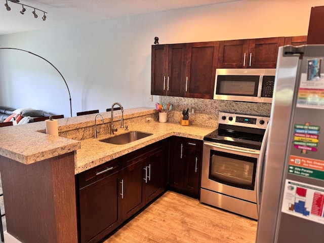 kitchen with dark brown cabinets, appliances with stainless steel finishes, light hardwood / wood-style floors, kitchen peninsula, and sink