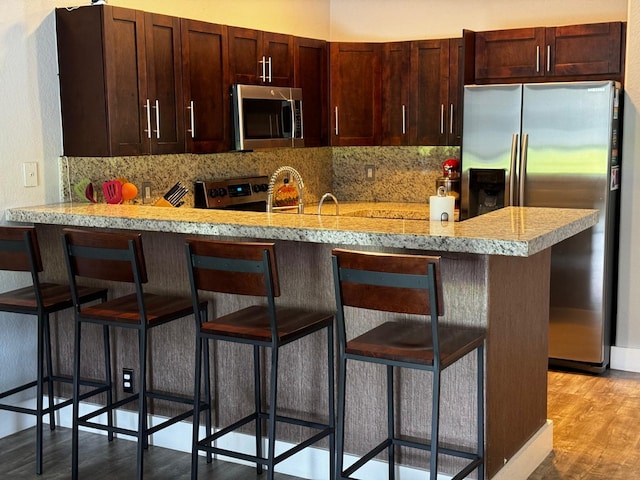 kitchen featuring light wood-type flooring, backsplash, stainless steel appliances, and a breakfast bar area