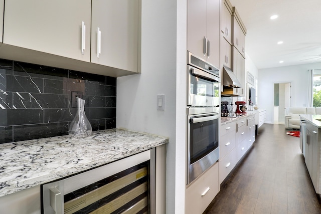 kitchen featuring backsplash, beverage cooler, dark hardwood / wood-style flooring, light stone countertops, and stainless steel double oven