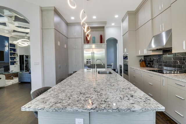 kitchen featuring sink, dark wood-type flooring, appliances with stainless steel finishes, light stone counters, and a center island with sink