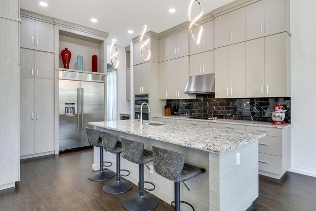 kitchen with appliances with stainless steel finishes, dark hardwood / wood-style floors, pendant lighting, tasteful backsplash, and a kitchen island with sink