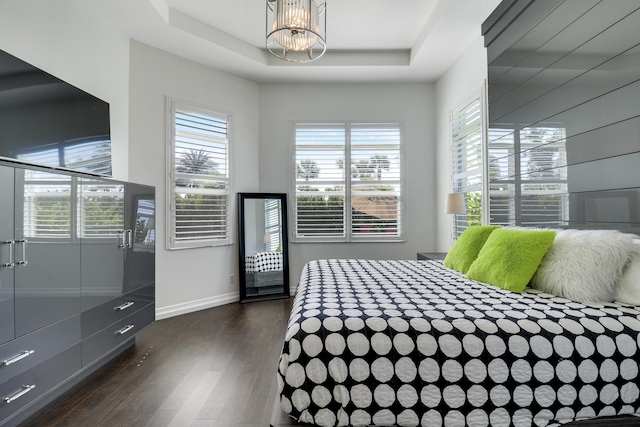 bedroom with dark hardwood / wood-style floors, an inviting chandelier, and a tray ceiling