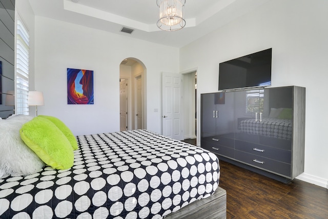 bedroom with an inviting chandelier, a tray ceiling, and dark hardwood / wood-style flooring