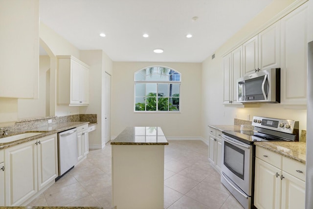 kitchen with light stone countertops, white cabinetry, a center island, stainless steel appliances, and light tile patterned floors