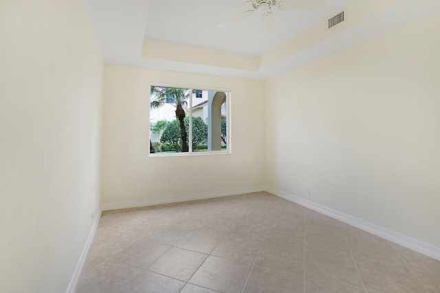 tiled empty room with ceiling fan and a tray ceiling