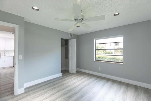 unfurnished bedroom with a textured ceiling, ceiling fan, light hardwood / wood-style flooring, and a closet