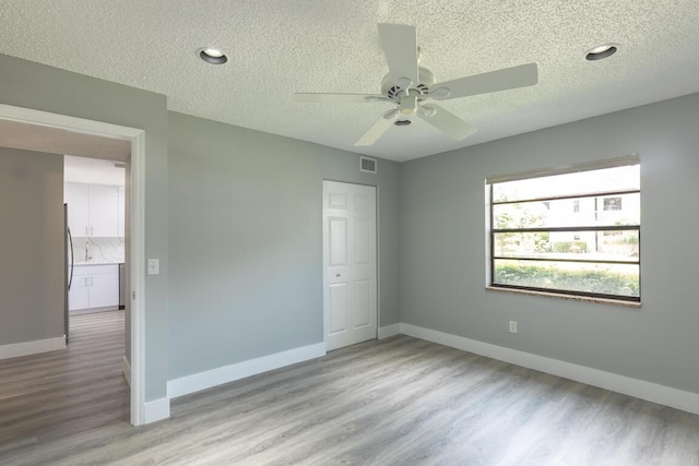 unfurnished bedroom with ceiling fan, stainless steel fridge, a textured ceiling, a closet, and light wood-type flooring