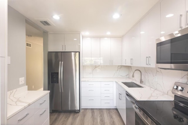 kitchen featuring sink, light stone countertops, light wood-type flooring, appliances with stainless steel finishes, and white cabinetry