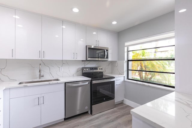 kitchen with sink, stainless steel appliances, light hardwood / wood-style flooring, decorative backsplash, and white cabinets