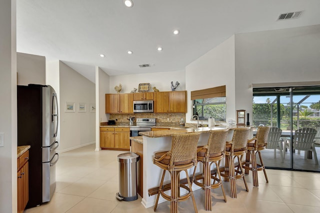 kitchen with light stone countertops, a kitchen bar, stainless steel appliances, decorative backsplash, and kitchen peninsula