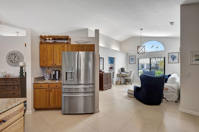 kitchen featuring vaulted ceiling, pendant lighting, light tile patterned floors, stainless steel fridge, and light stone counters