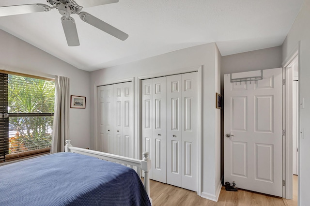 bedroom featuring vaulted ceiling, ceiling fan, two closets, and light hardwood / wood-style flooring