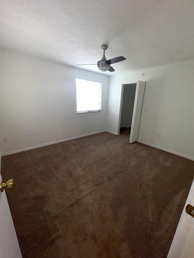 spare room featuring ceiling fan, a textured ceiling, and dark colored carpet