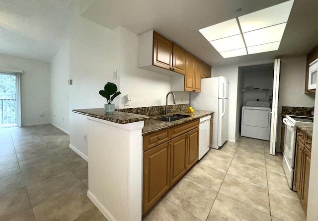 kitchen featuring white appliances, washer / clothes dryer, dark stone countertops, kitchen peninsula, and sink