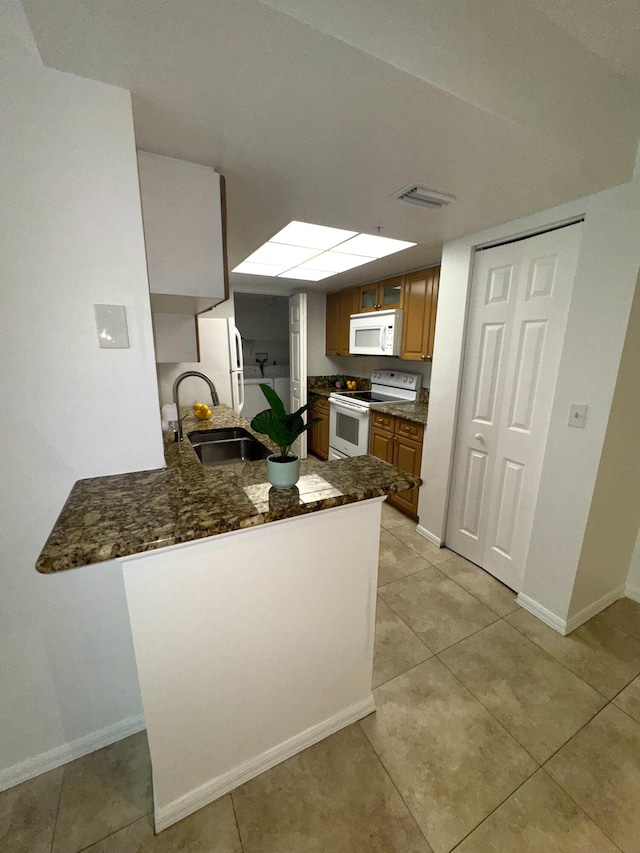 kitchen featuring sink, light tile patterned floors, dark stone countertops, kitchen peninsula, and white appliances