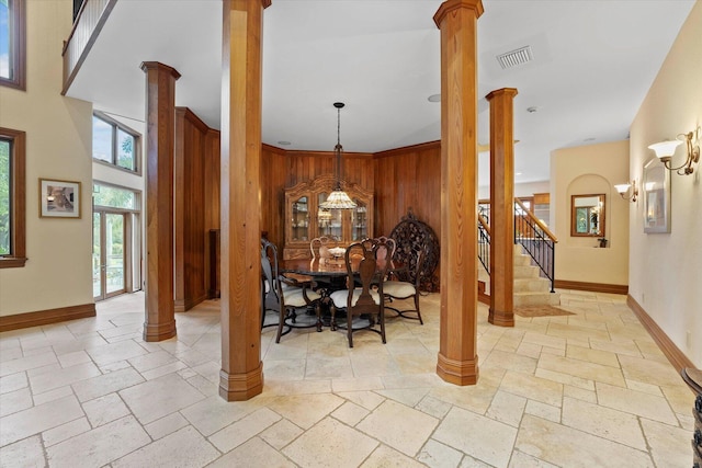 dining space featuring a notable chandelier, a towering ceiling, wooden walls, and decorative columns