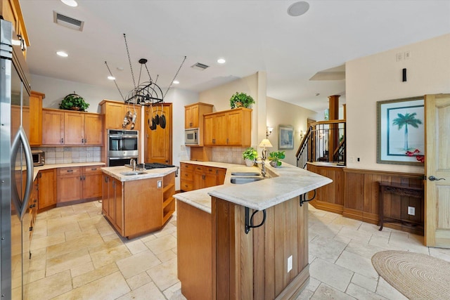 kitchen featuring kitchen peninsula, appliances with stainless steel finishes, tasteful backsplash, sink, and an island with sink