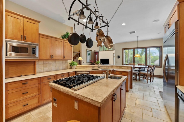 kitchen featuring pendant lighting, a kitchen island with sink, sink, built in appliances, and decorative backsplash