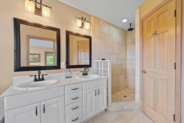 bathroom with tile patterned flooring, vanity, a tile shower, and a textured ceiling