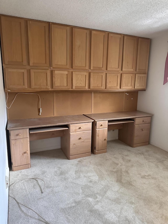 unfurnished office with built in desk, light colored carpet, and a textured ceiling