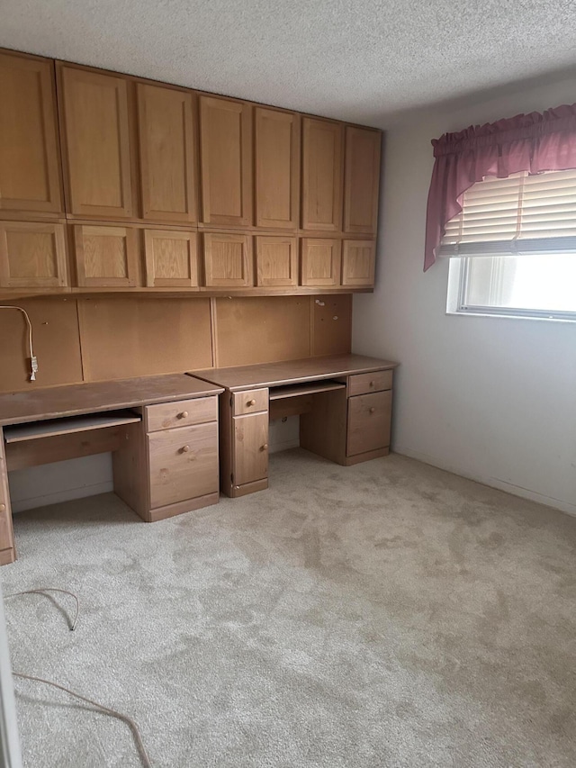 unfurnished office featuring a textured ceiling, built in desk, and light colored carpet