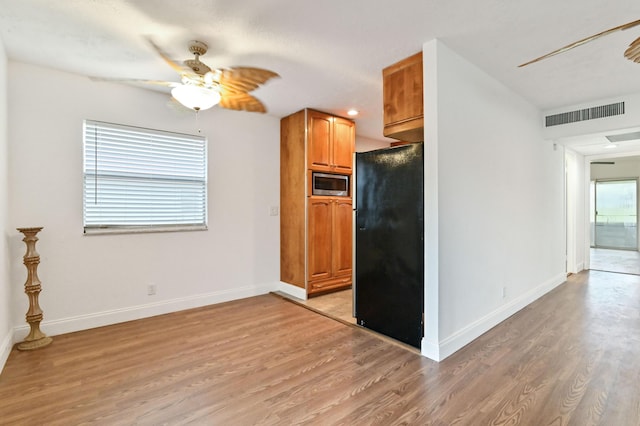 kitchen with black refrigerator, light hardwood / wood-style flooring, stainless steel microwave, and ceiling fan