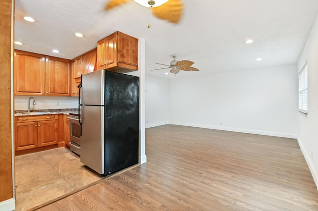 kitchen with light stone countertops, ceiling fan, sink, stainless steel appliances, and light hardwood / wood-style floors